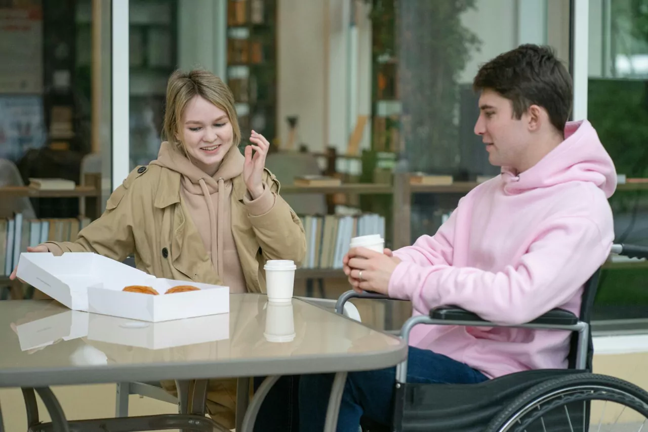 A young man in a wheelchair sharing a meal with a friend at a cafe